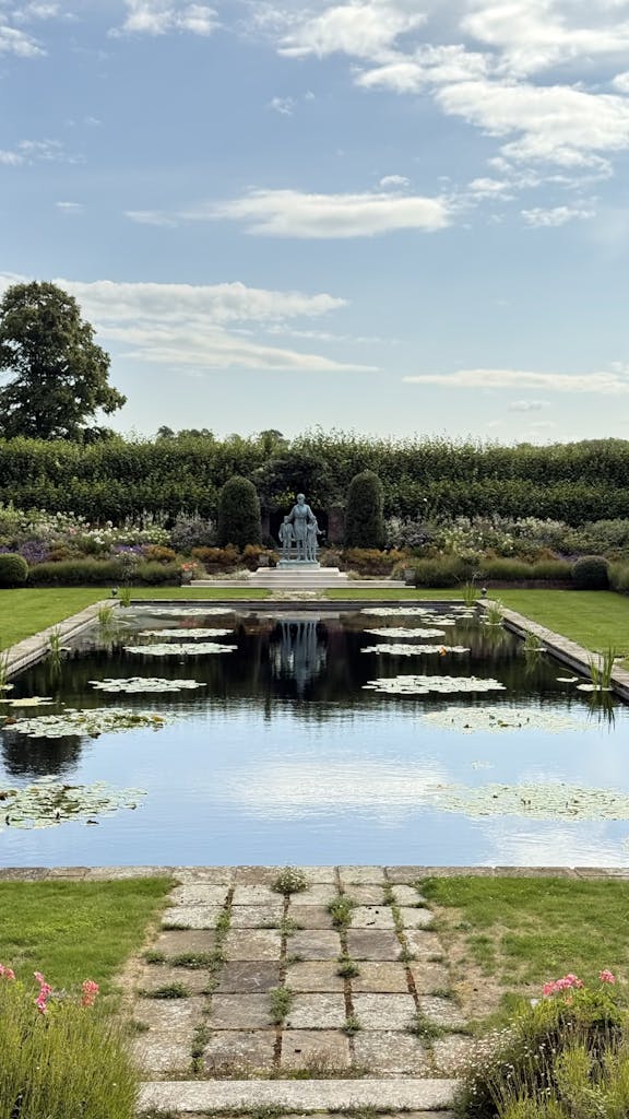 Tranquil garden pond with lily pads and a statue under a blue sky in London.